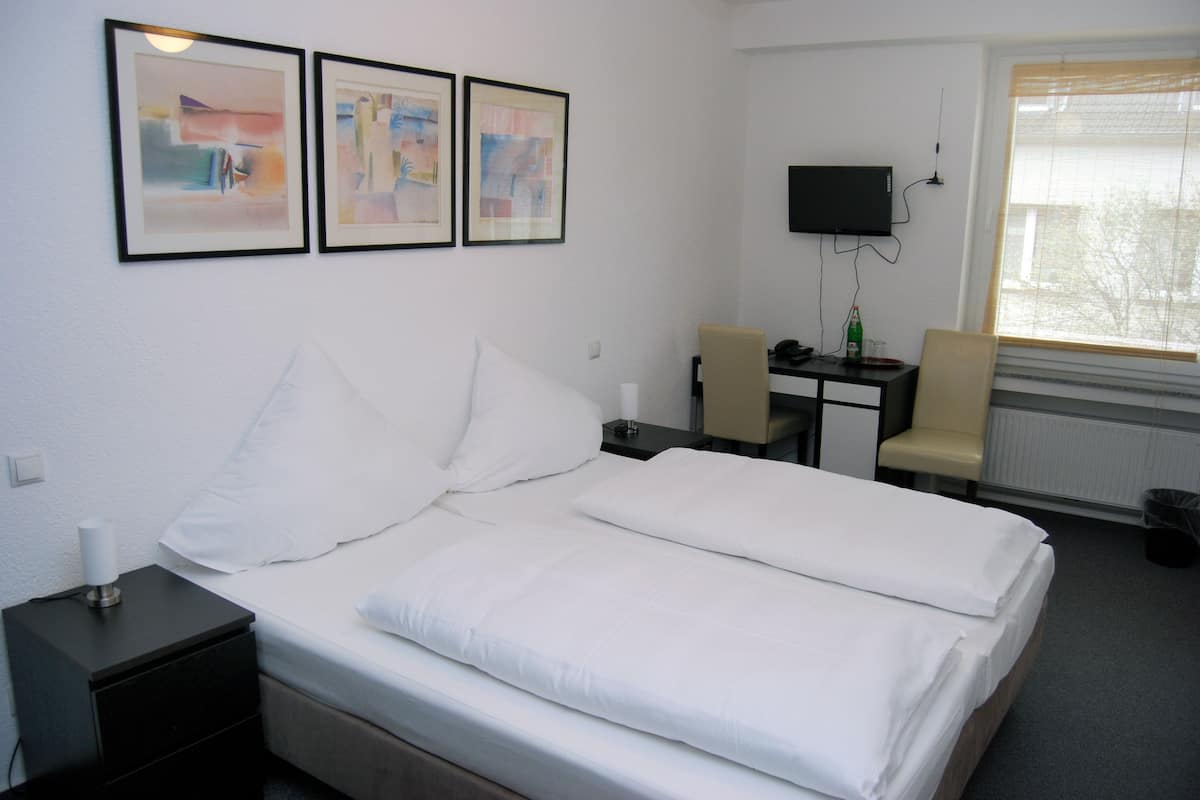 A hotel room with a bed, a desk, a chair, and a TV on the wall.