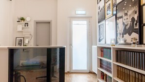 A hallway with a white door, a black chair, and a bookshelf filled with books. - TM Hotel Düsseldorf (Düsseldorf)