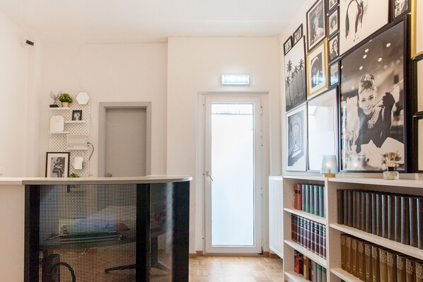 A hallway with a white door, a black chair, and a bookshelf filled with books. - TM Hotel Düsseldorf (Düsseldorf)
