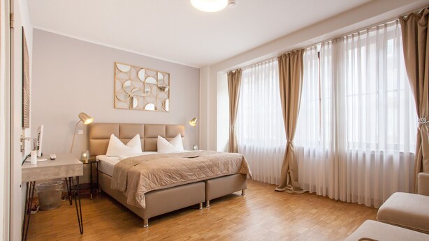 A modern bedroom with a bed, bedside tables, a desk, and a large window with curtains. - TM Hotel Düsseldorf (Düsseldorf)