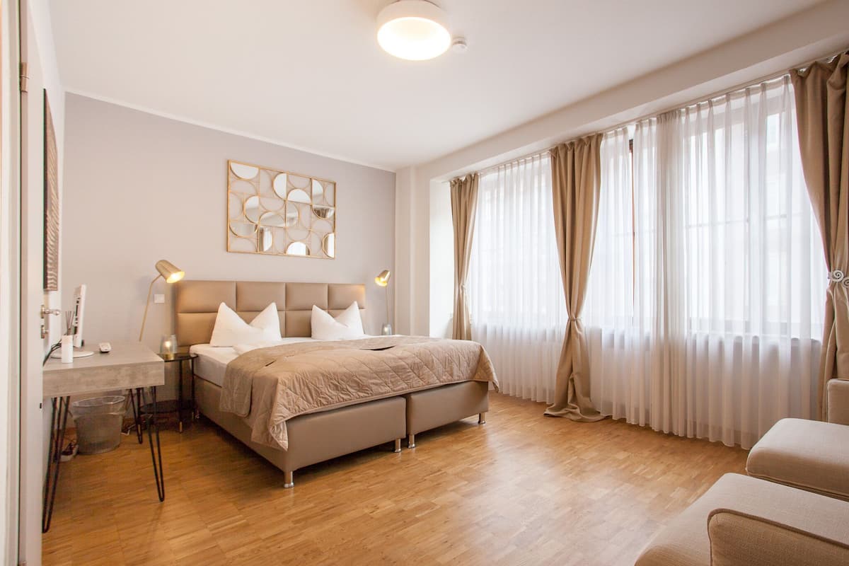 A modern bedroom with a bed, bedside tables, a desk, and a large window with curtains.
