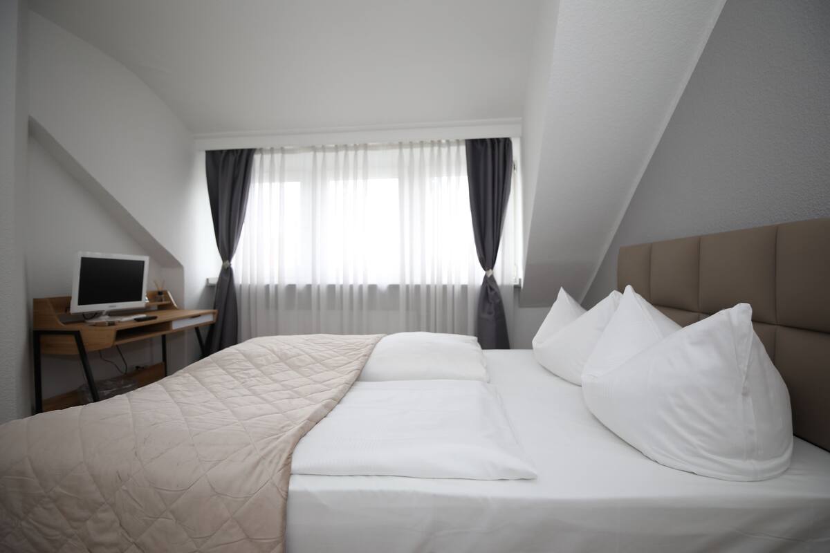 A neatly arranged bedroom with a bed, a desk, and a computer.