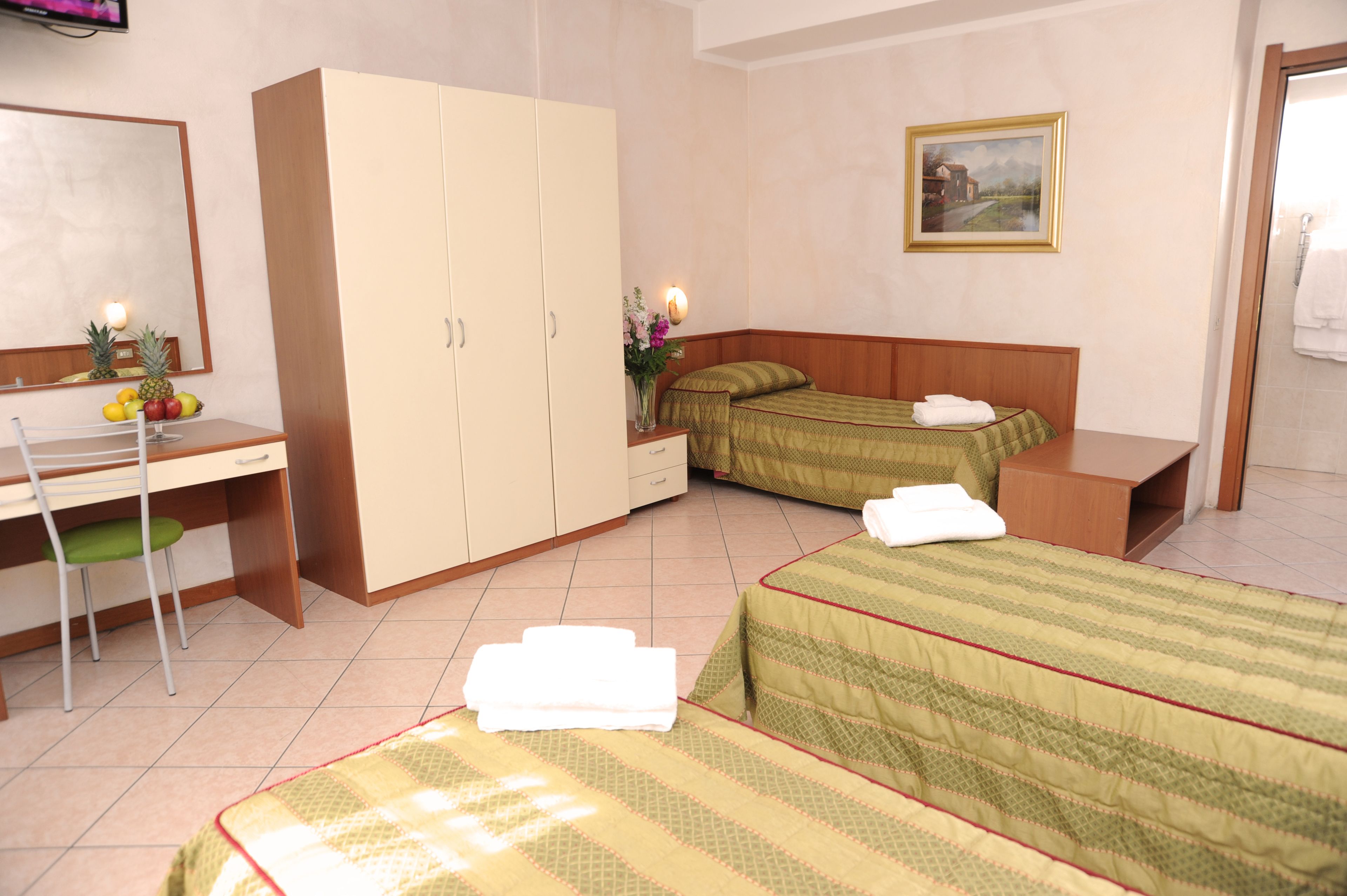 A hotel room with a desk, two beds, a wardrobe, and a painting on the wall.