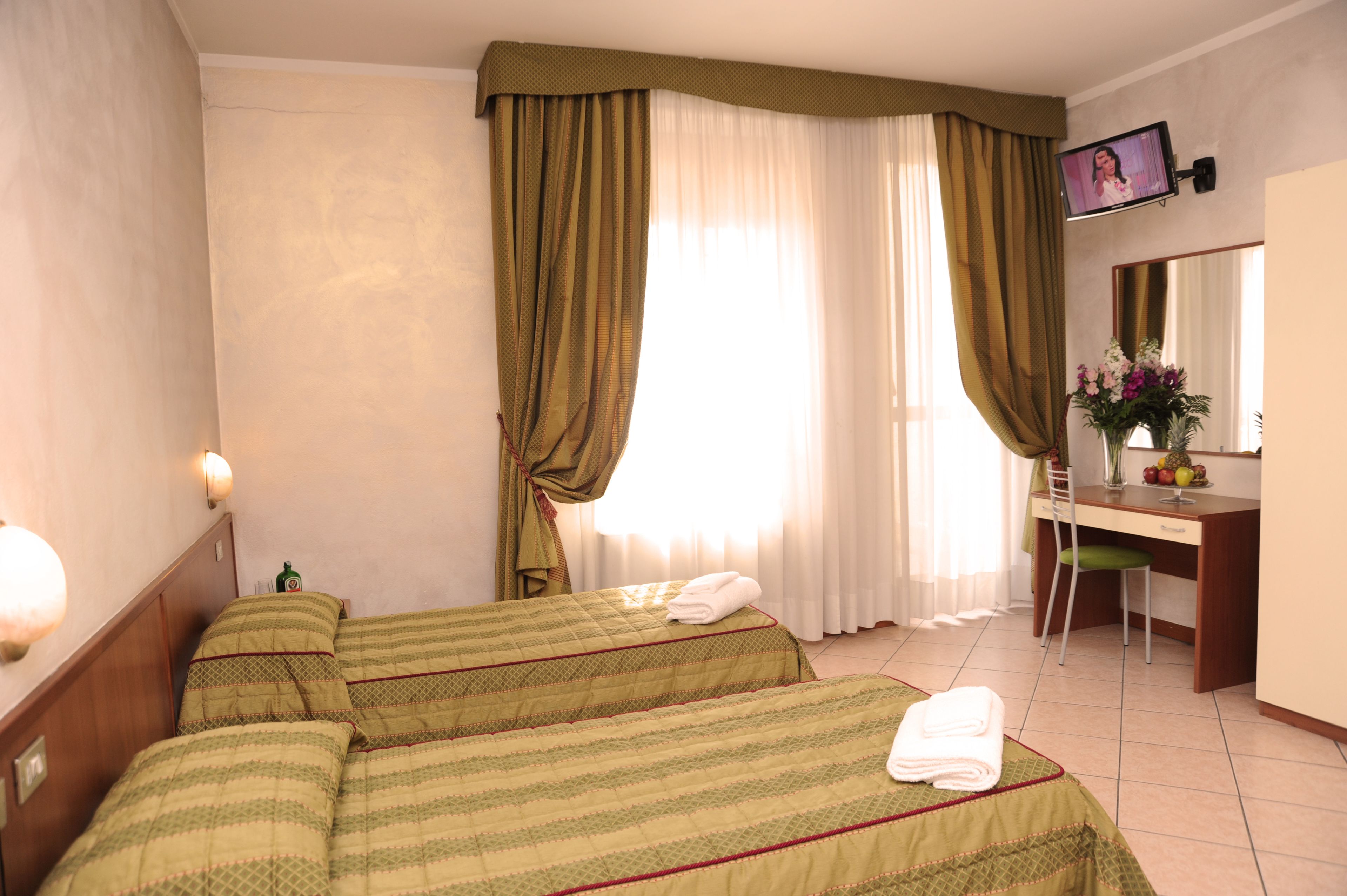 A hotel room with two beds, a desk, a chair, a TV, and a mirror.