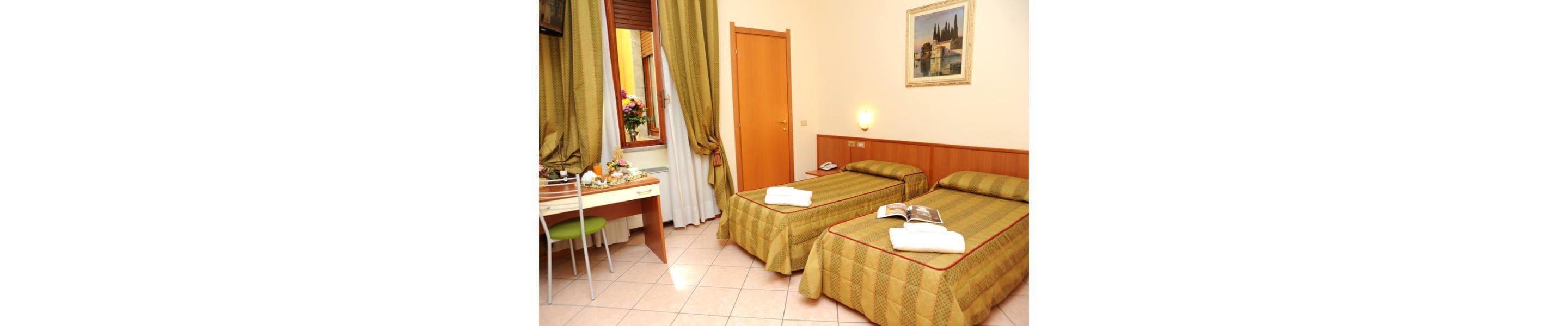 A hotel room with two beds, a desk, a chair, a mirror, a door, and a painting on the wall.
