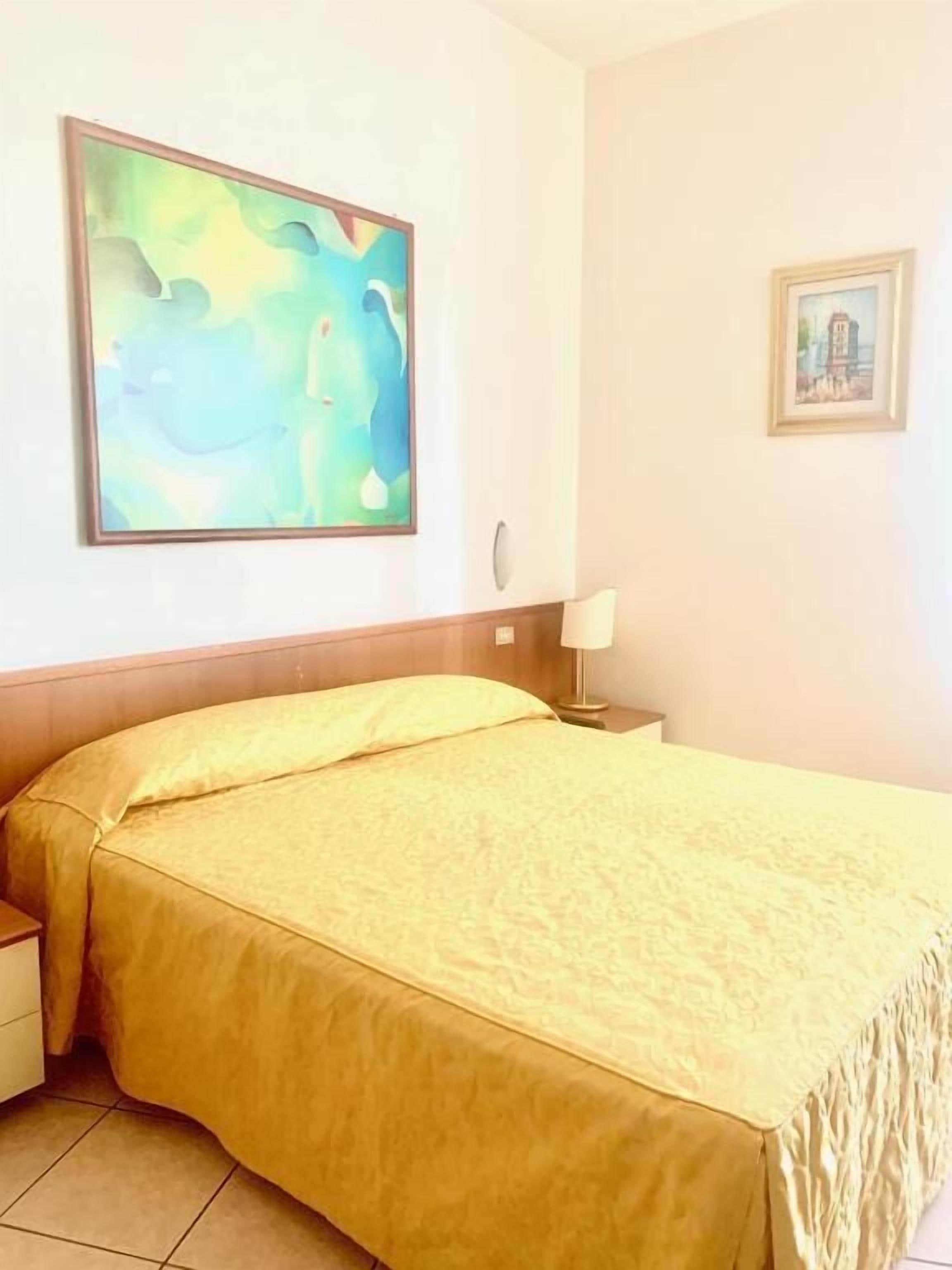 A hotel room with a bed, a nightstand, a lamp, and two framed pictures on the wall.