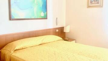 A hotel room with a bed, a nightstand, a lamp, and two framed pictures on the wall.