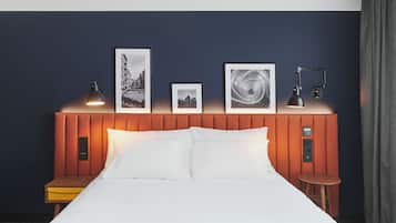 Habitación de hotel con cama, lámparas de noche, mesita de noche y panel de control en la pared.