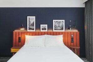 Habitación de hotel con cama, lámparas de noche, mesita de noche y panel de control en la pared.
