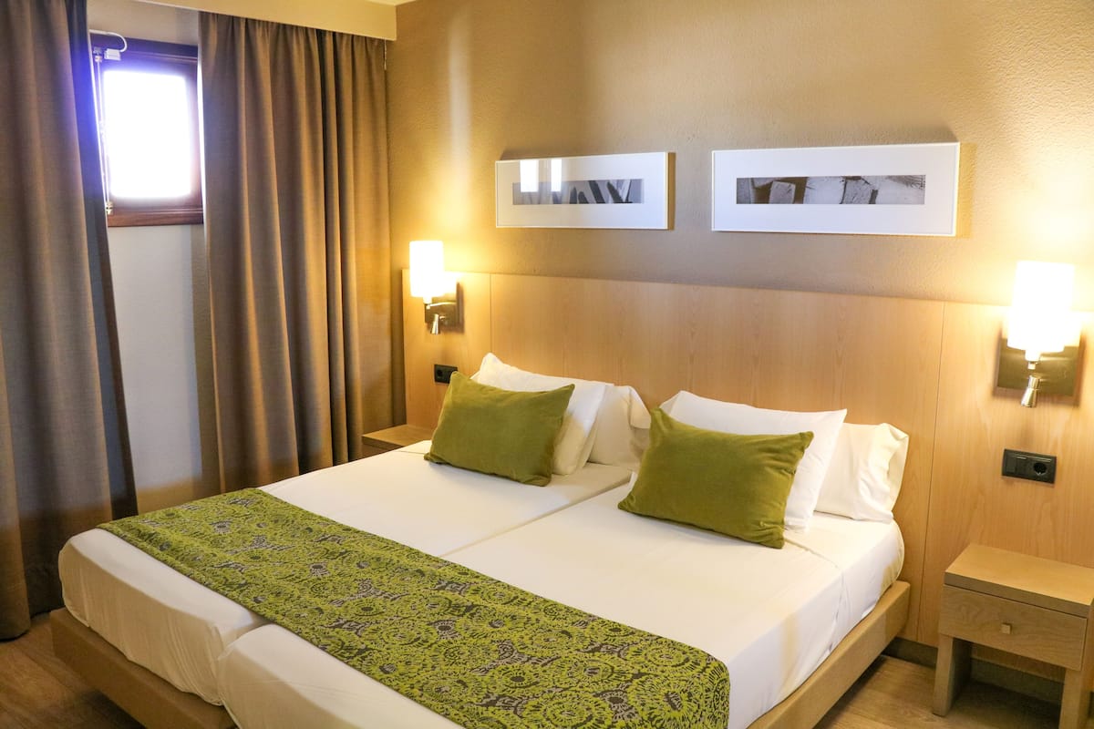 Una cama doble con ropa de cama verde y blanca, dos lámparas fijadas a la pared y dos cuadros colgados.