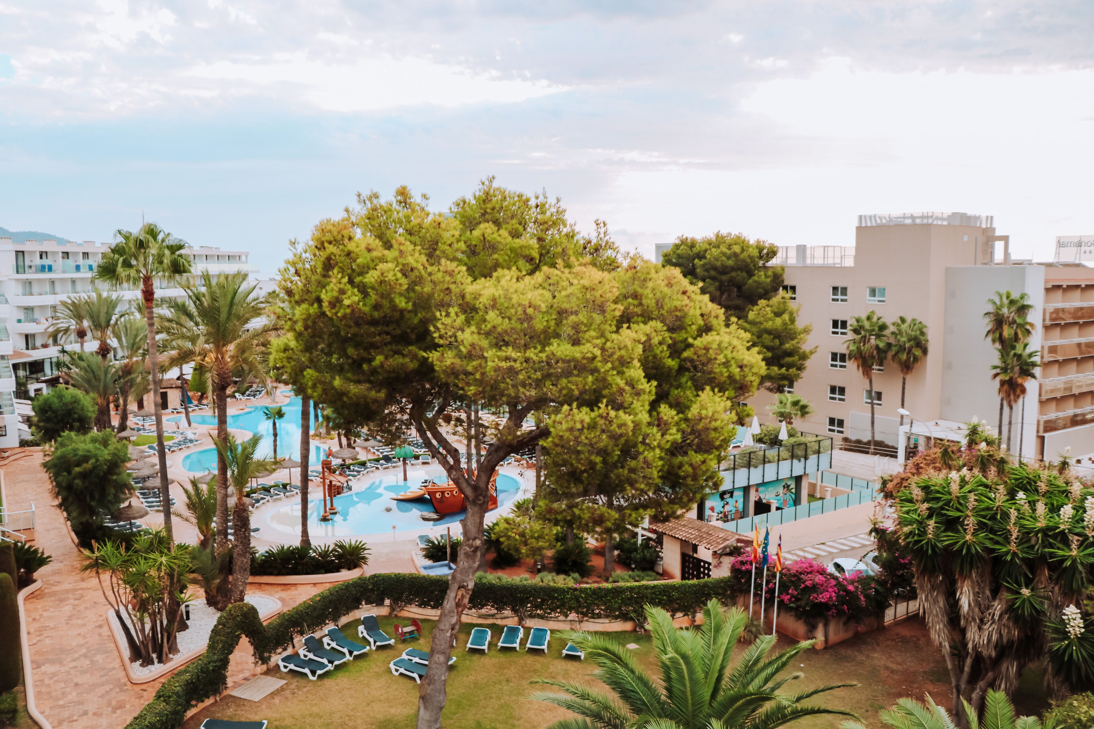 Et resort med swimmingpool, palmer og udsigt til de omkringliggende bygninger.