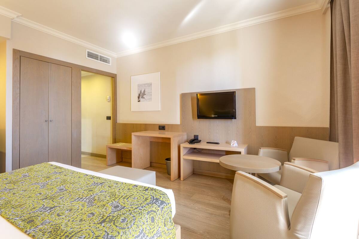 Una habitación de hotel con una cama, un escritorio, una silla, un televisor y una mesita.