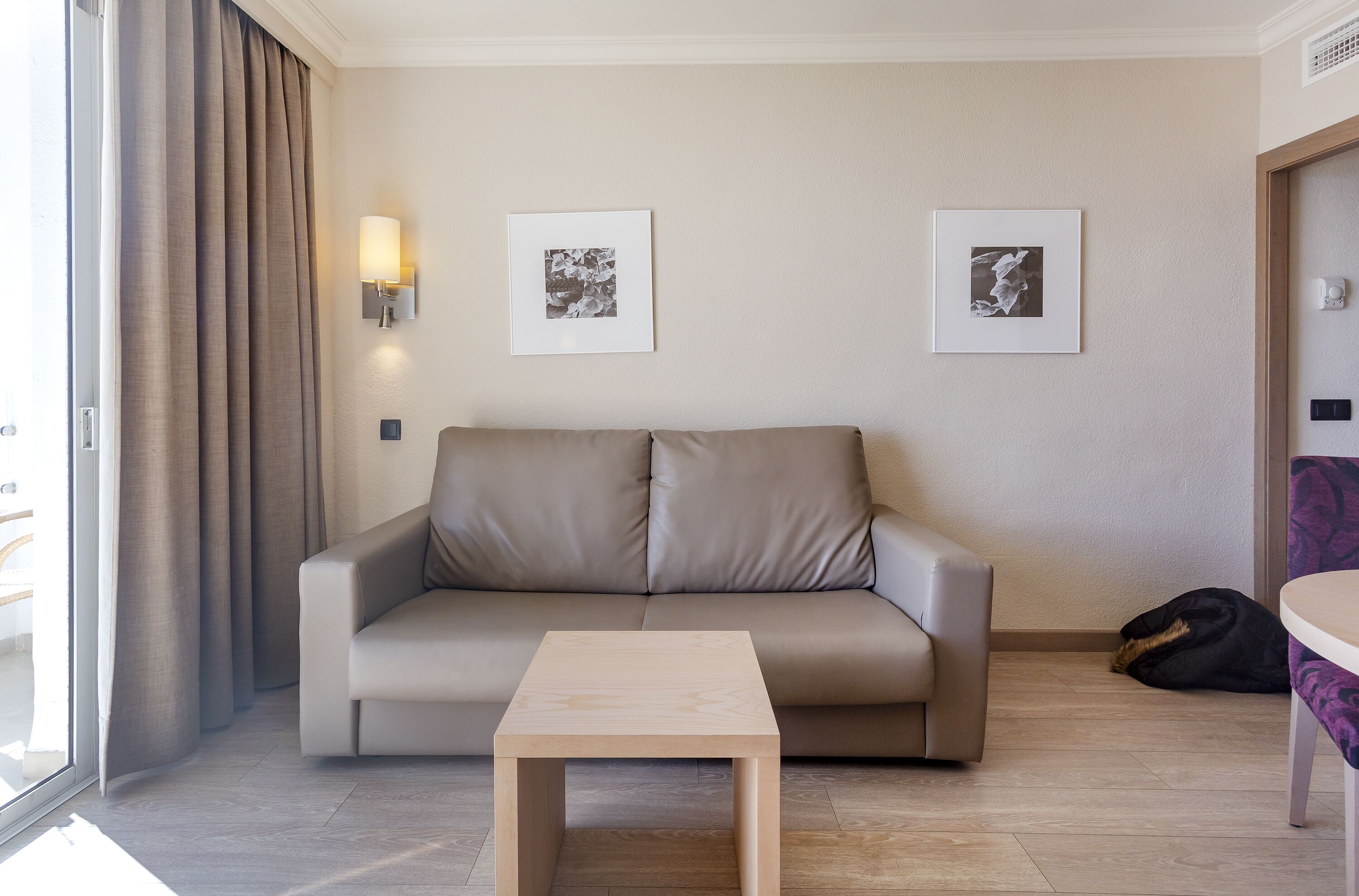 A modern hotel room with a beige sofa, a small wooden table, and two framed pictures on the wall.