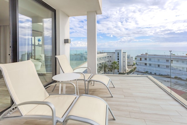 A balcony with two chairs and a small table, overlooking a cityscape and the sea.