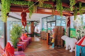 A room with a wooden ceiling, hanging plants, a large polar bear statue, and a colorful striped sofa. - Marins Playa (Son Servera)