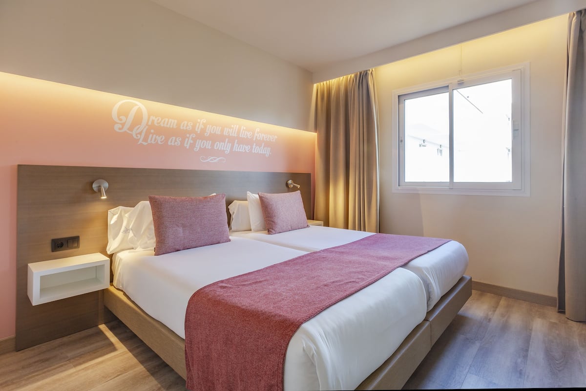 Una habitación de hotel moderna con una cama grande, mesitas de noche, un estante en la pared y un ventanal con cortinas.