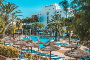 Un resort con piscina, tumbonas y sombrillas de paja.