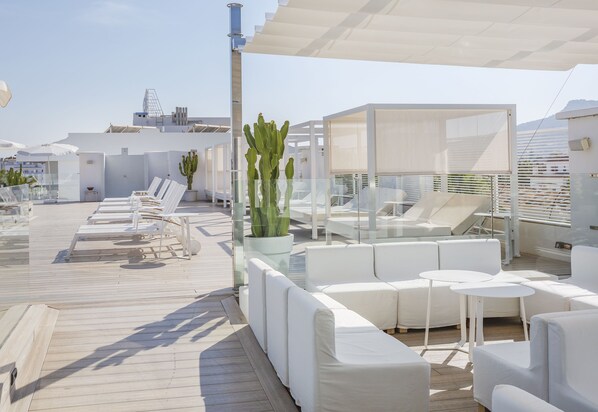 Un lounge en la azotea con mobiliario blanco, incluyendo sofás y sillones, y una gran planta de cactus.