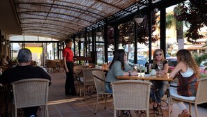 An outdoor cafe with wicker furniture, a covered seating area, and a view of the street. - Hotel Bell Port (Capdepera)