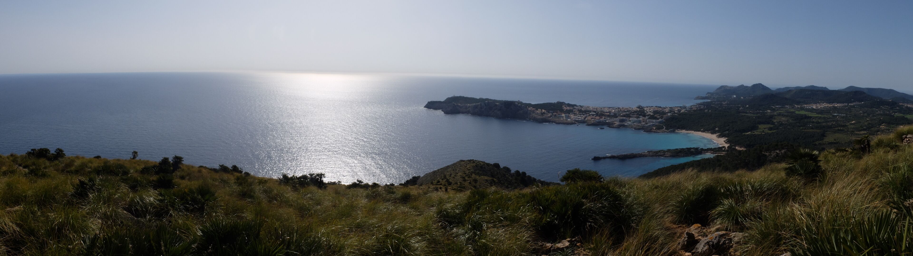 Un paisaje costero con vista despejada al mar, un pueblo pequeño y terreno montañoso.