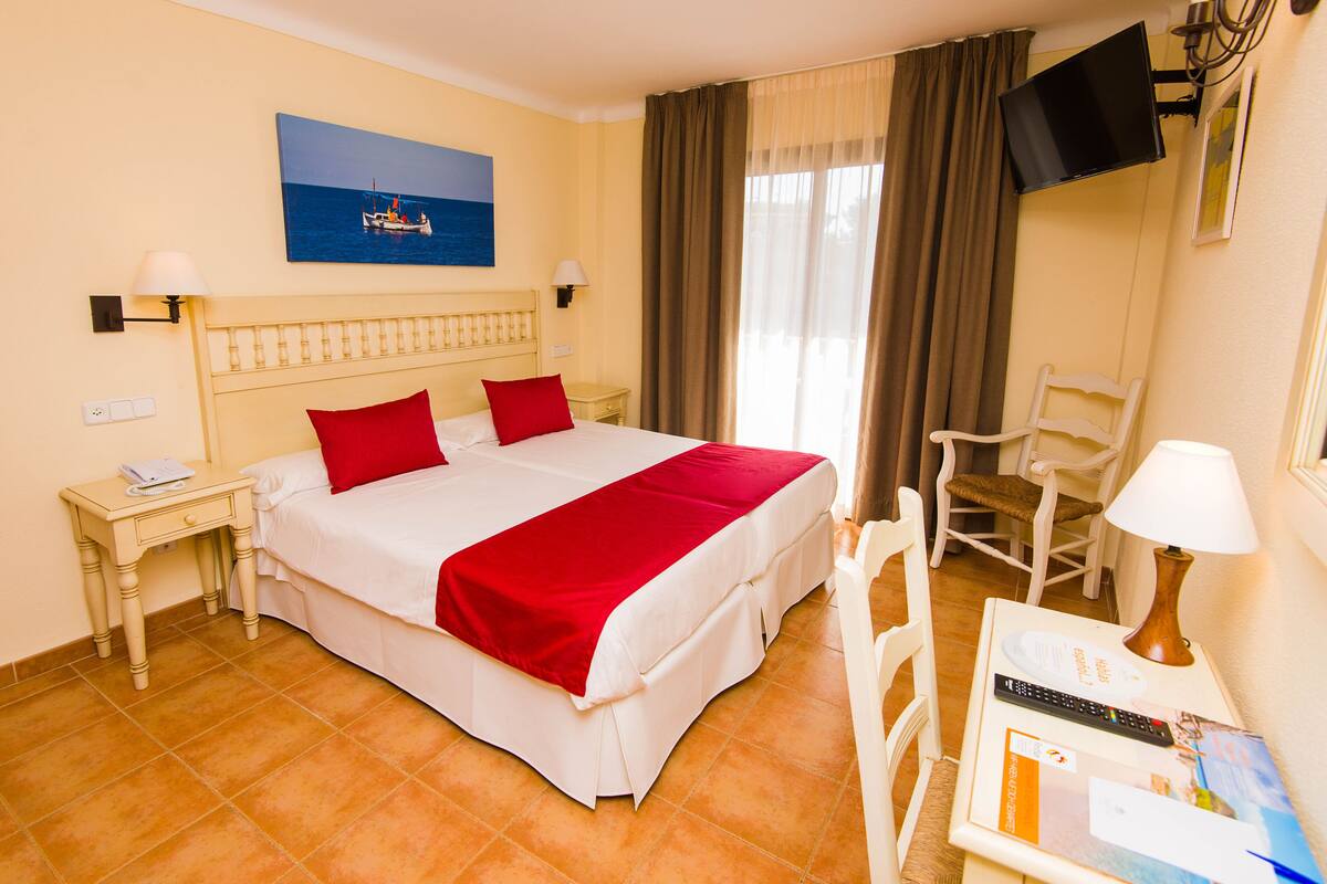 A hotel room with a bed, a nightstand, a chair, a TV, and a painting on the wall.