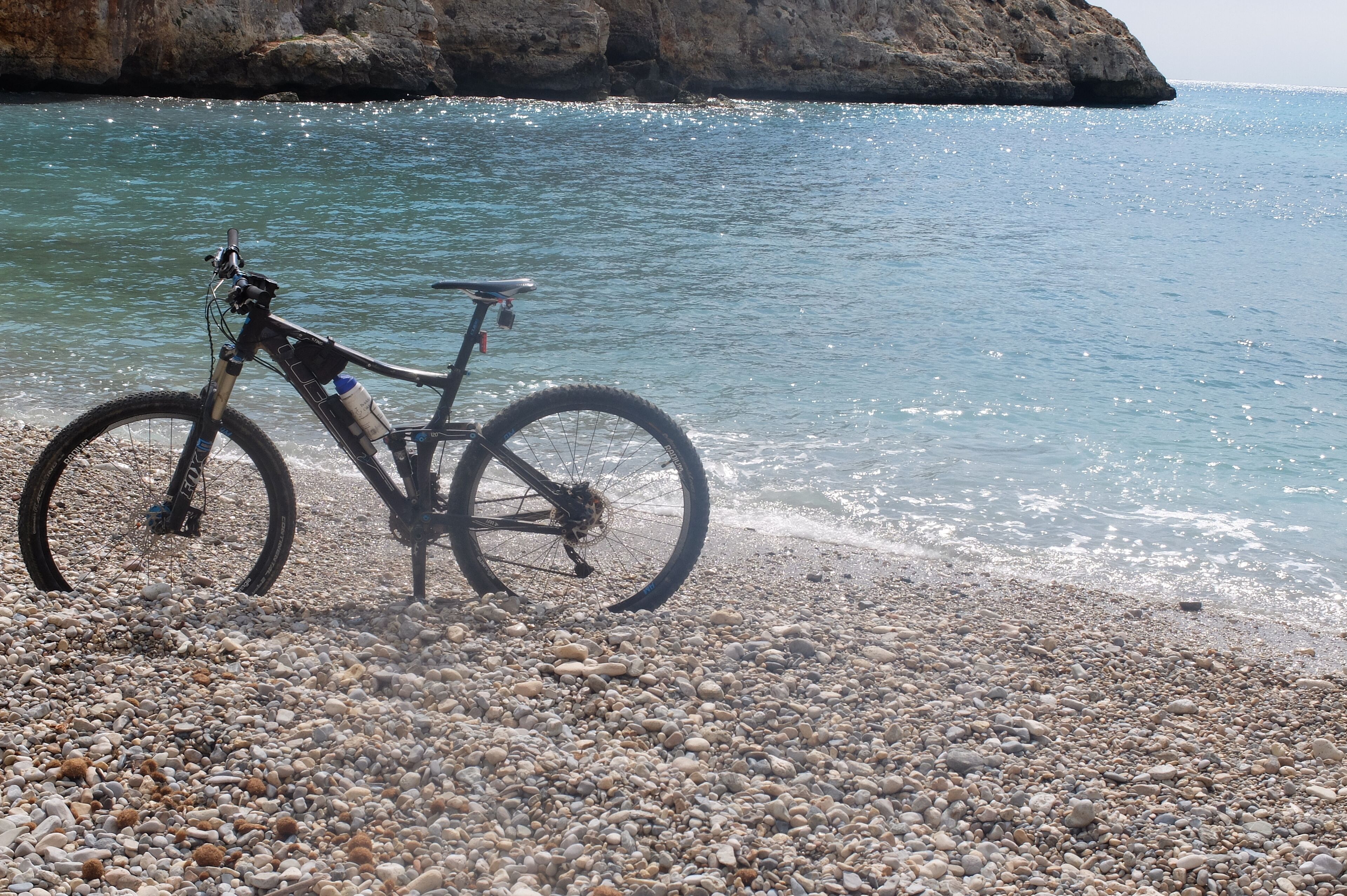 A bicycle parked on a pebbled beach with a rocky cliff in the background.