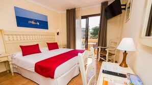 A hotel room with a bed, a desk with a lamp, a TV, and a balcony with chairs. - Hotel Bell Port (Capdepera)