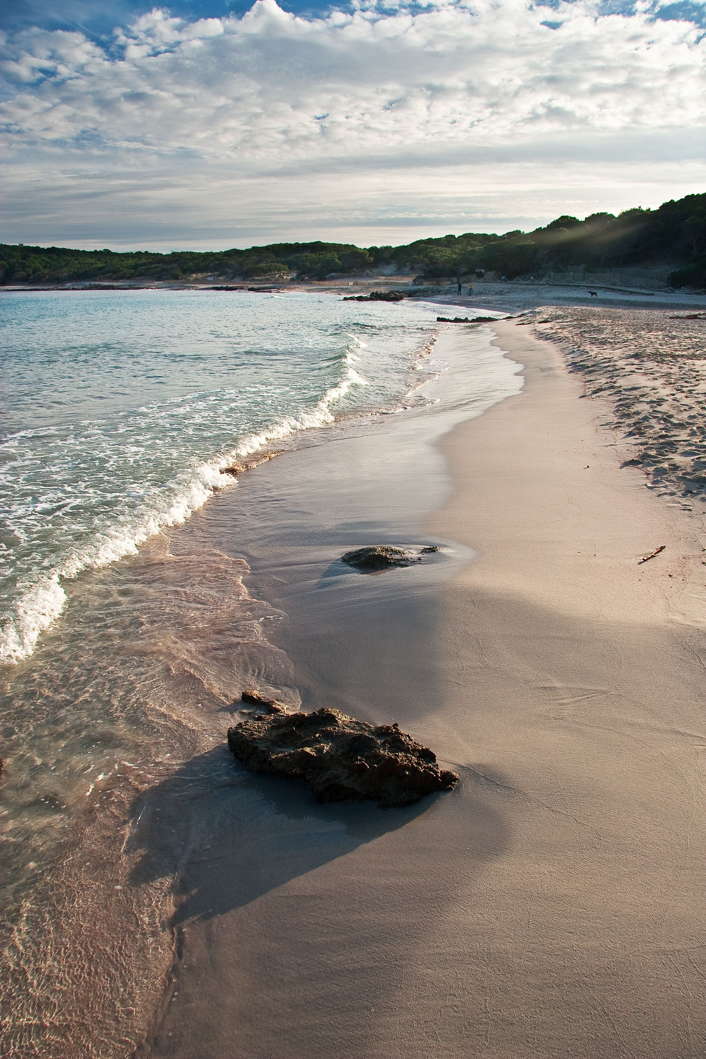 Une plage à l’eau claire, avec un rivage sablonneux et un promontoire rocheux.