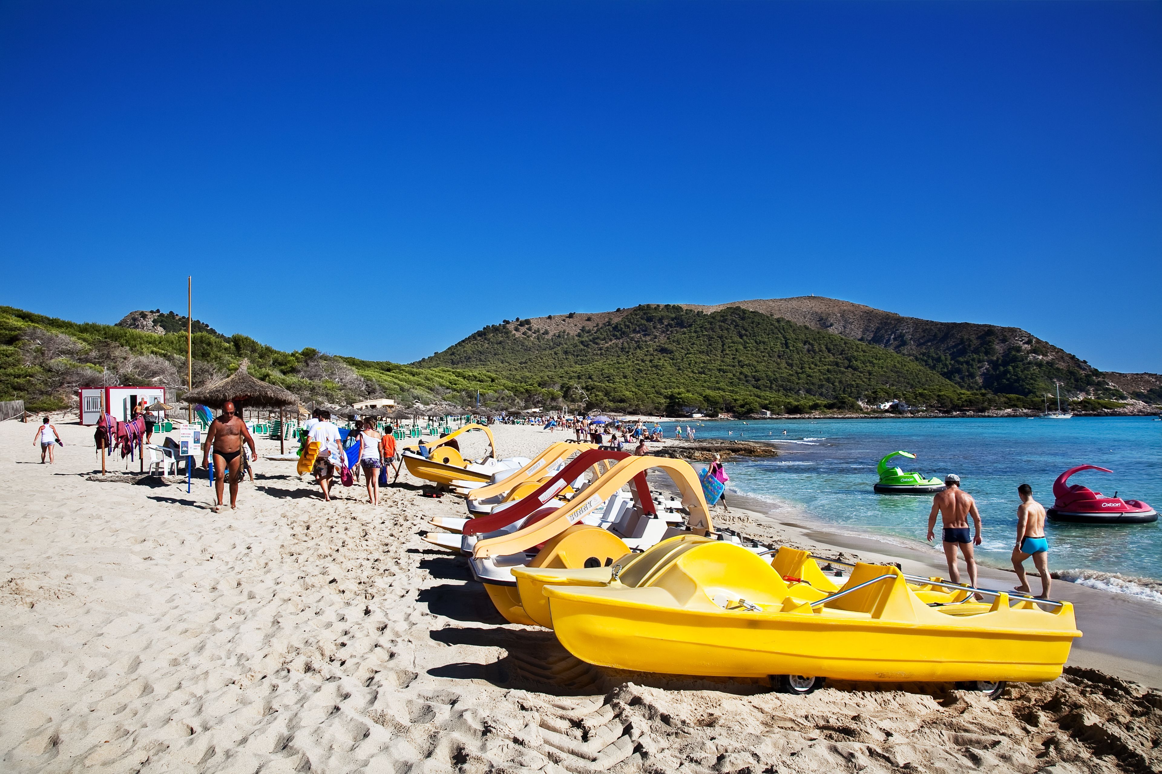 A beach with yellow boats and people walking.