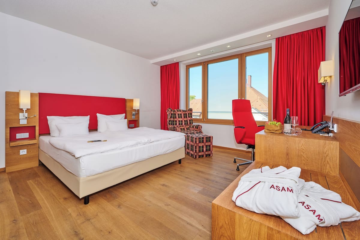 Quarto de hotel com uma cama grande, cortinas vermelhas, uma escrivaninha de madeira e vista para a praia.