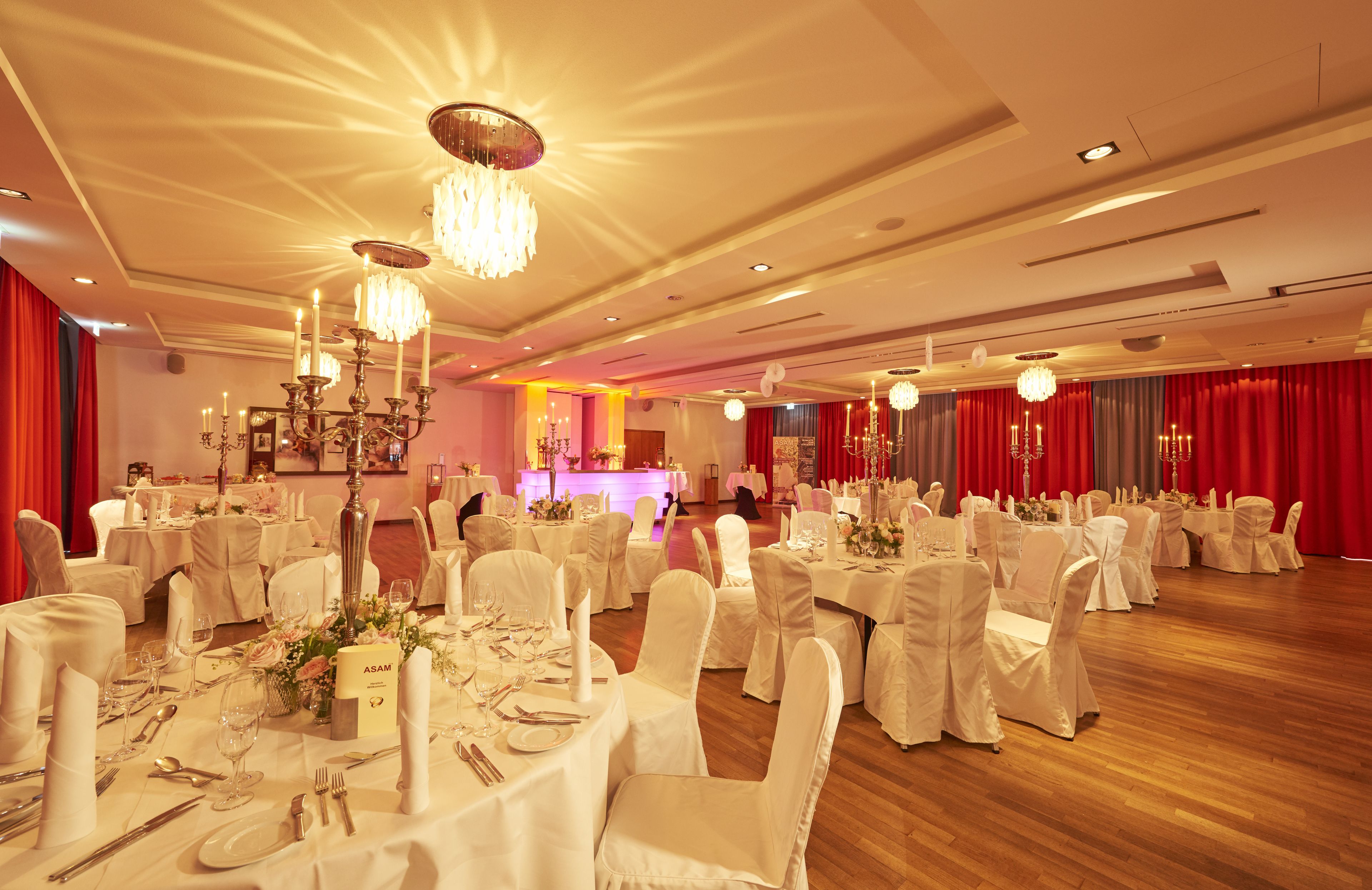 A banquet hall with round tables, white tablecloths, and chandeliers.