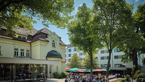 A courtyard with a crowd of people, outdoor seating, and a building with a green dome.