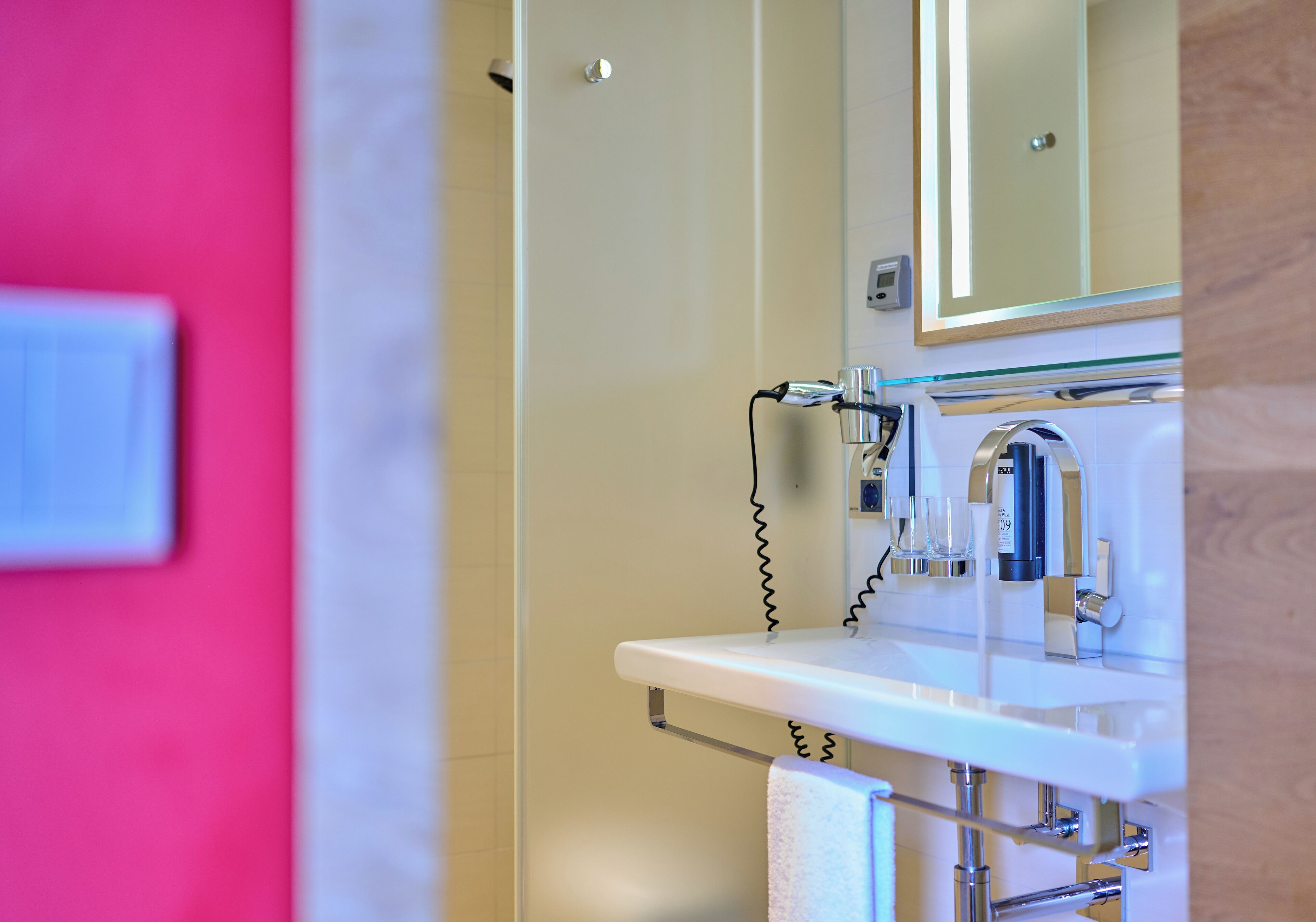 Un baño con lavamanos blanco, un espejo y zona de ducha.