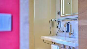 Un baño con lavamanos blanco, un espejo y zona de ducha.