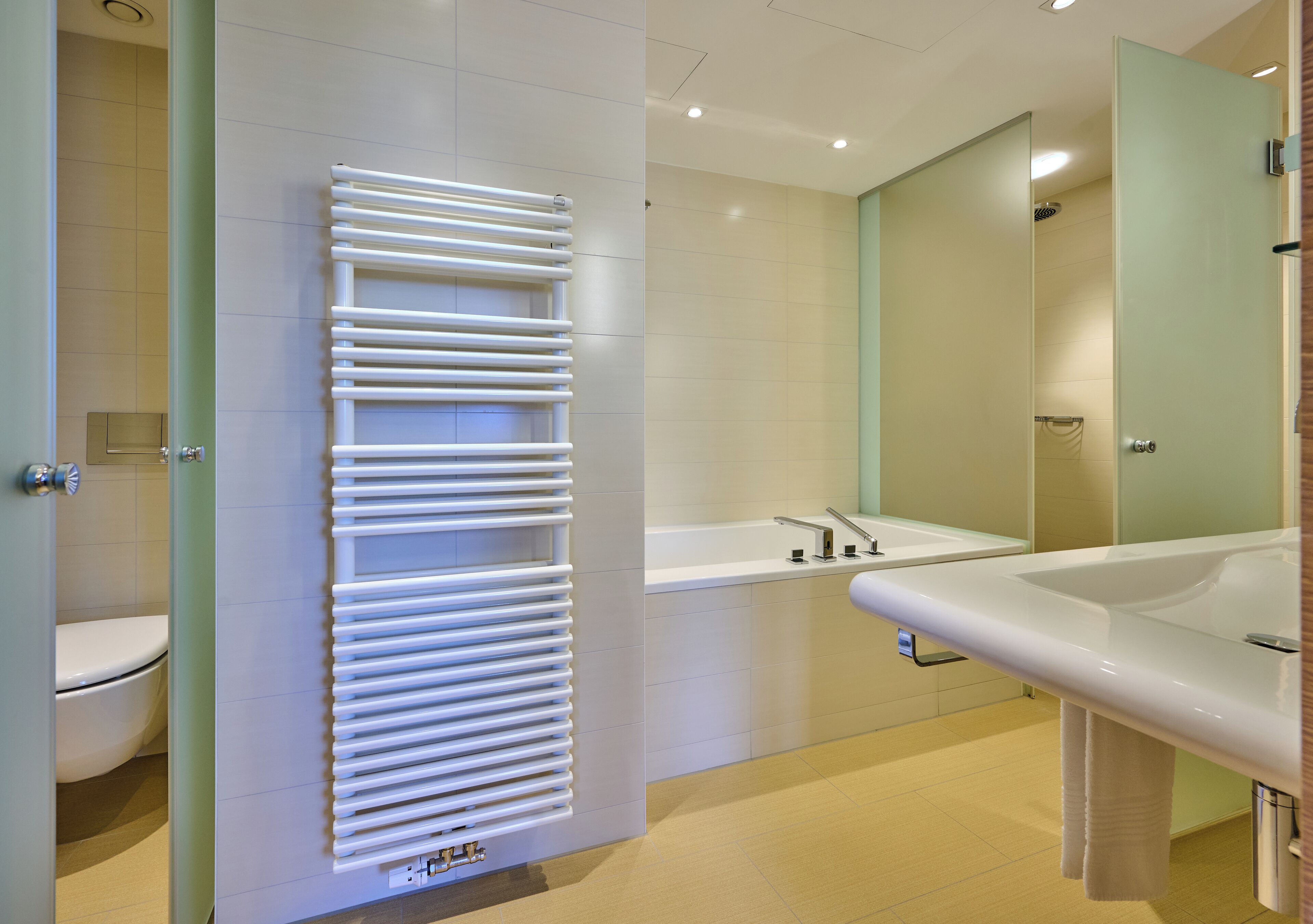 Een moderne badkamer met een douchecabine van glas, een wit wastafeltje en een toilet.