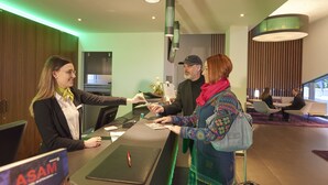 A reception desk with a sign for ASAM, a modern interior with wooden paneling, and a seating area with two people in the background.