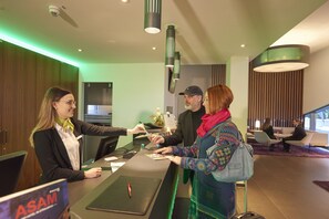 A reception desk with a sign for ASAM, a modern interior with wooden paneling, and a seating area with two people in the background.