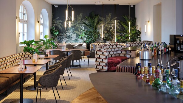 Zona de bar moderna con asientos, barra y un mural de plantas tropicales.