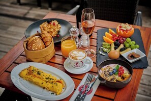 A breakfast setting with croissants, an omelette, a bowl of yogurt with berries, a glass of orange juice, and a wine glass.