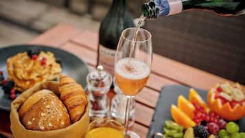 Une table dressée pour le petit-déjeuner avec des croissants, un verre de jus d’orange, une bouteille de champagne et une assiette de fruits.