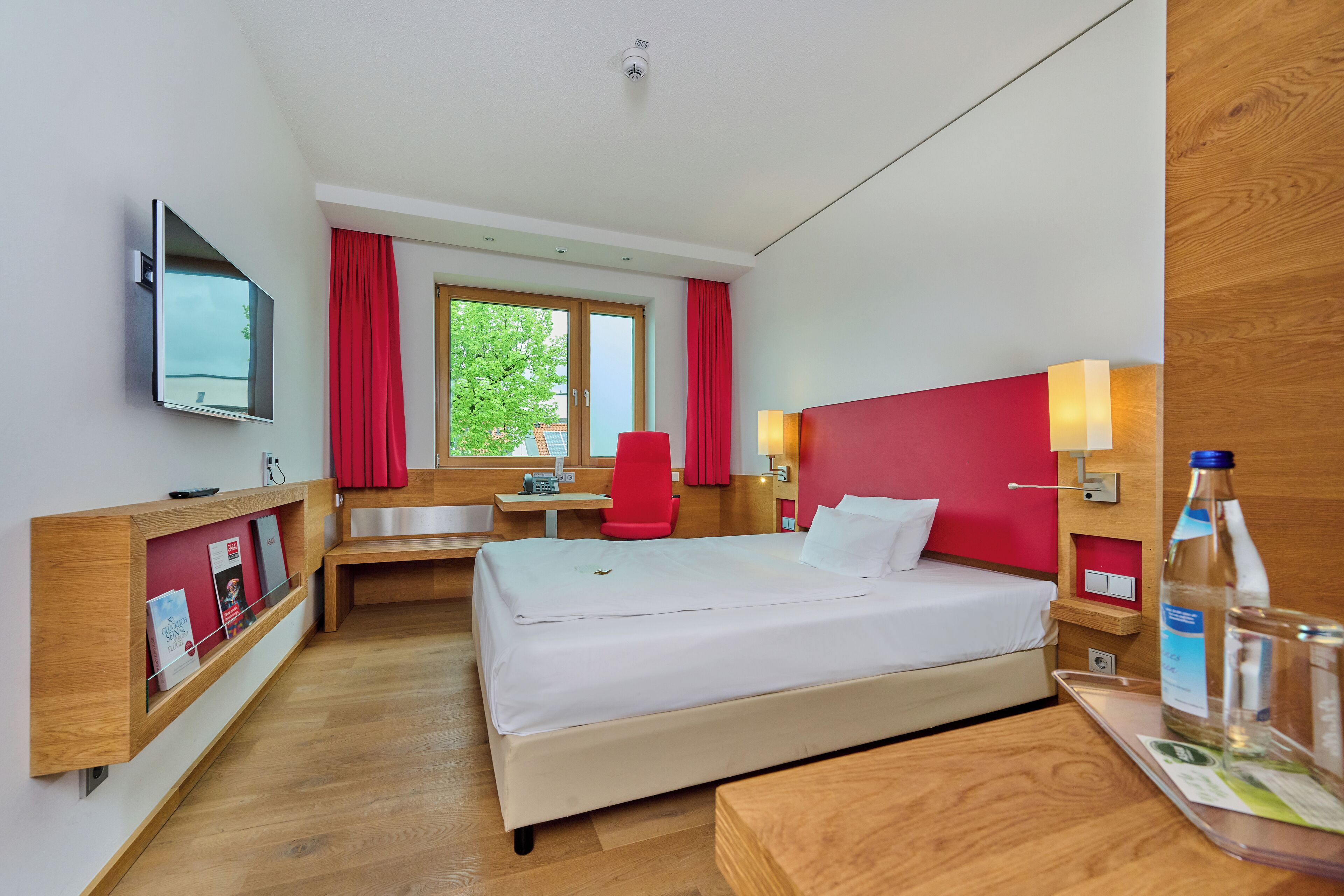 A hotel room with a bed, desk, chair, TV, and a window with curtains.