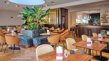 A modern restaurant with round tables, cushioned seating, and a large plant centerpiece.