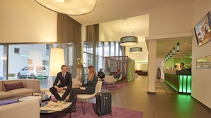 Un moderno vestíbulo de hotel con zonas de estar, una recepción y una escalera que conduce a los pisos superiores.