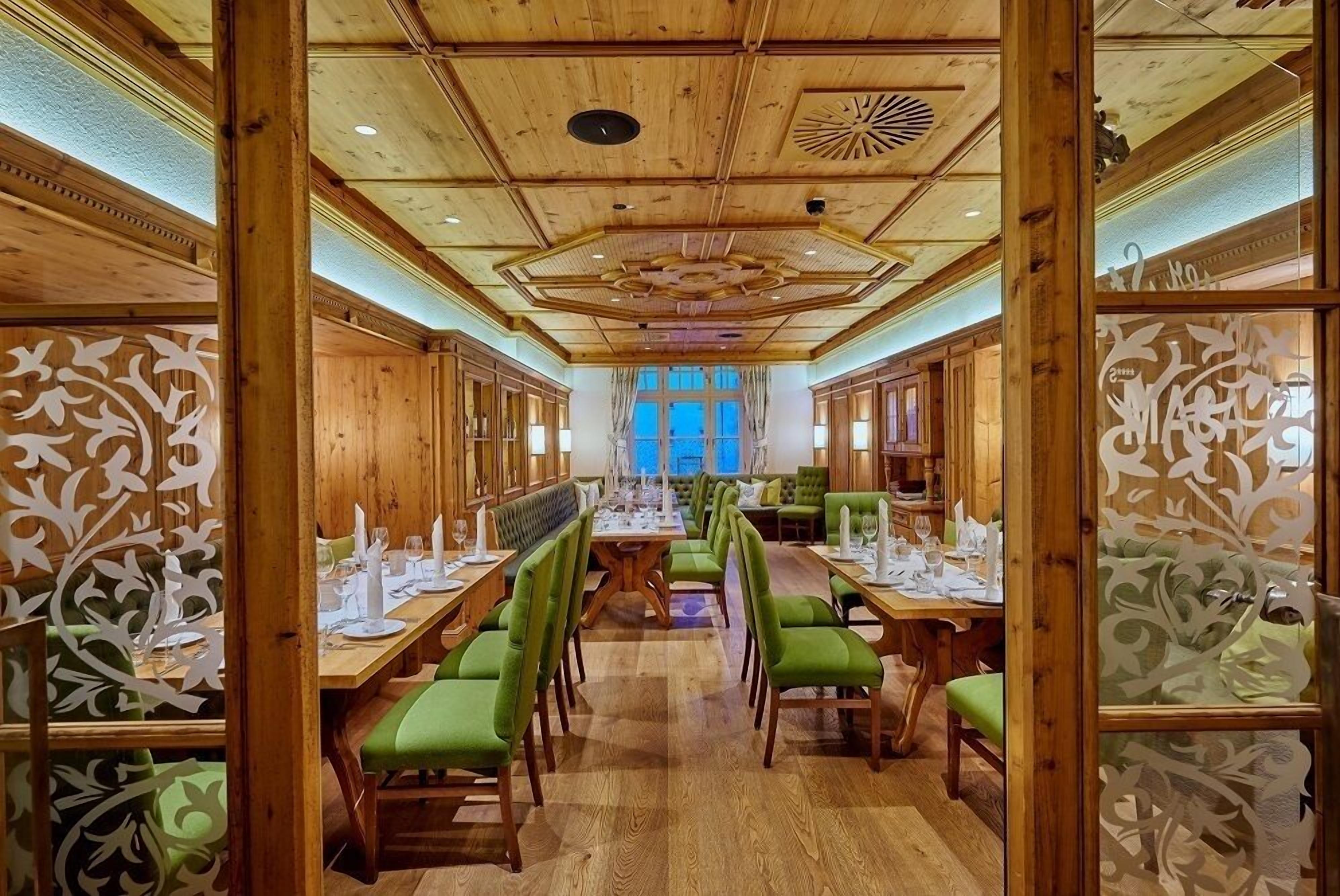Un restaurant au décor intérieur en bois, avec des chaises à revêtement vert et une grande table à manger placée au centre de la salle, prête pour le repas.