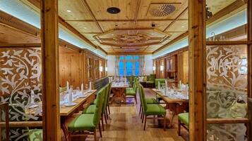 Un restaurante con interiores de madera, sillas tapizadas en verde y una mesa central dispuesta para una comida.