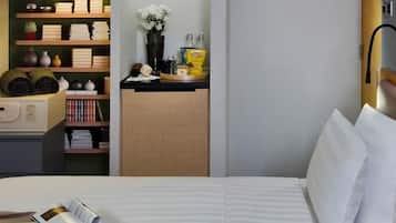 A neatly organized hotel room with a bed, a small desk, and a shelf with books and decorative items.