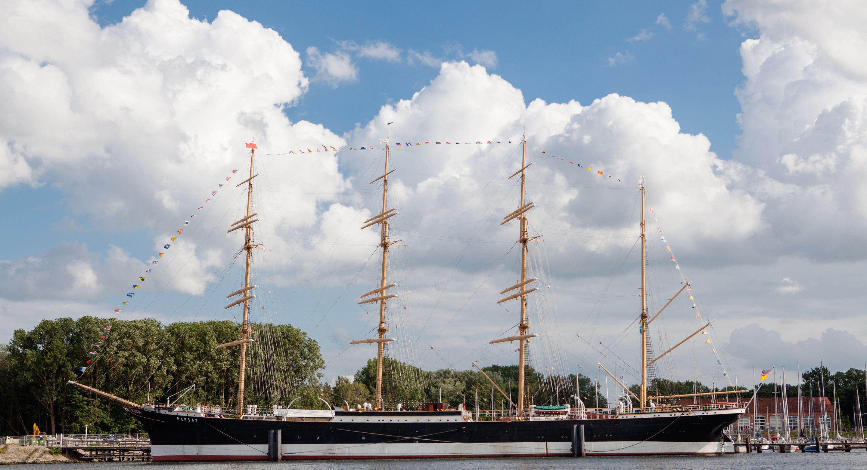 Un grand voilier était amarré dans une marina, sous un ciel dégagé parsemé de quelques nuages.