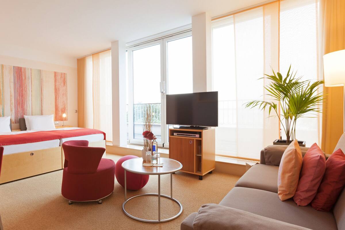 Habitación de hotel con cama, televisor, escritorio, silla, sofá y planta.