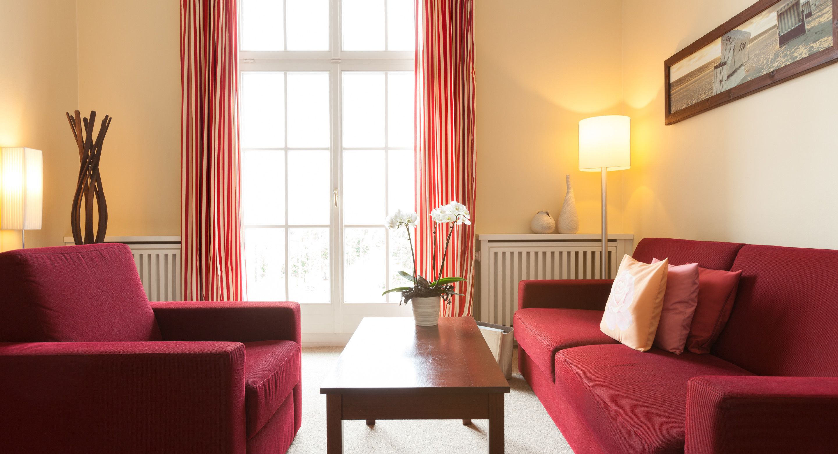 A room with a red sofa, a matching armchair, a wooden coffee table, and a potted plant.