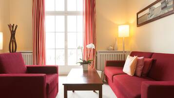 A room with a red sofa, a matching armchair, a wooden coffee table, and a potted plant.